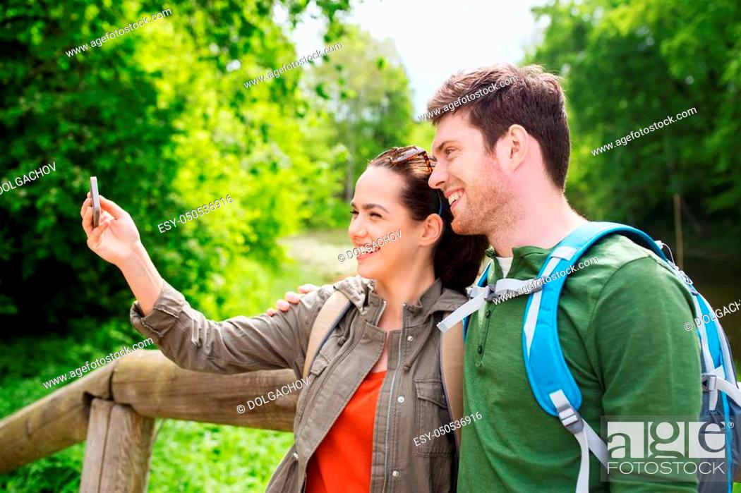 Stock Photo: travel, hiking, backpacking, tourism and people concept - smiling couple with backpacks taking selfie by smartphone in nature.