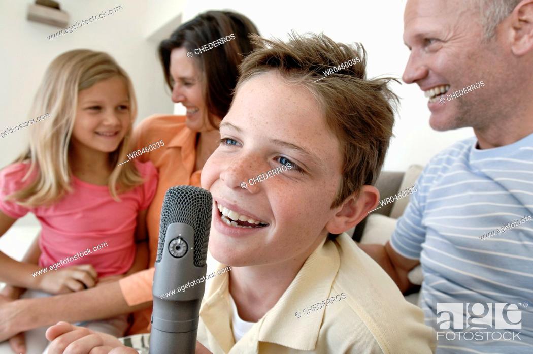 Stock Photo: Close-up of a boy singing into a microphone with his family sitting beside him.