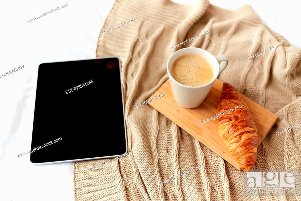 Stock Photo: technology, coziness, morning and winter concept - tablet pc computer, coffee cup and croissant on bed at home.