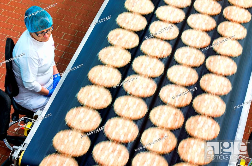 Stock Photo: An employee supervises the adding of toppings to frozen pizzas at a production line in the pizza plant of food manufacturer Dr.