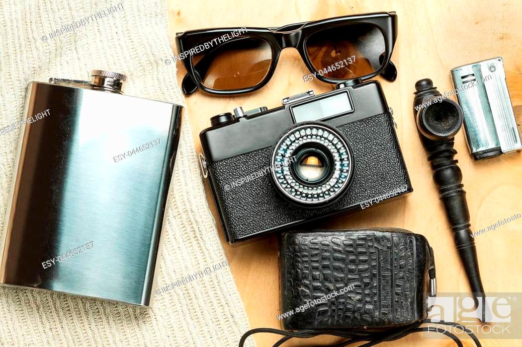Stock Photo: Accessories of the creative person. 35-mm film camera, exposure meter in leather case, steel flask, sunglasses and smoking set on wooden background.