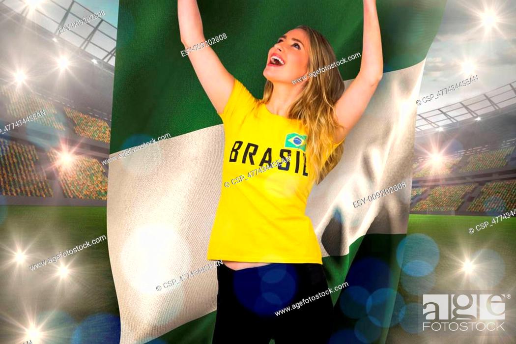 Stock Photo: Excited football fan in brasil tshirt holding nigeria flag against large football stadium with lights.