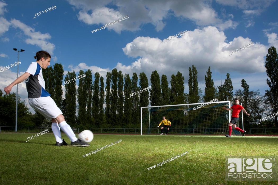 Stock Photo: Full length of young soccer player kicking ball towards goal post.