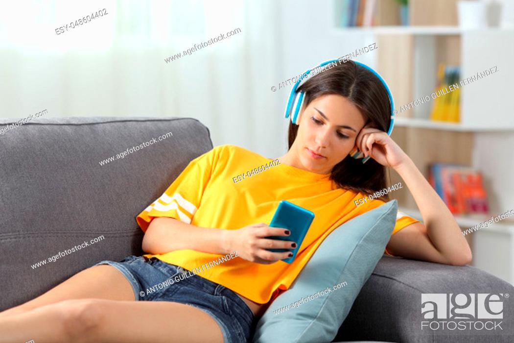 Stock Photo: Relaxed girl in yellow listening to music sitting on a couch in the living room at home.