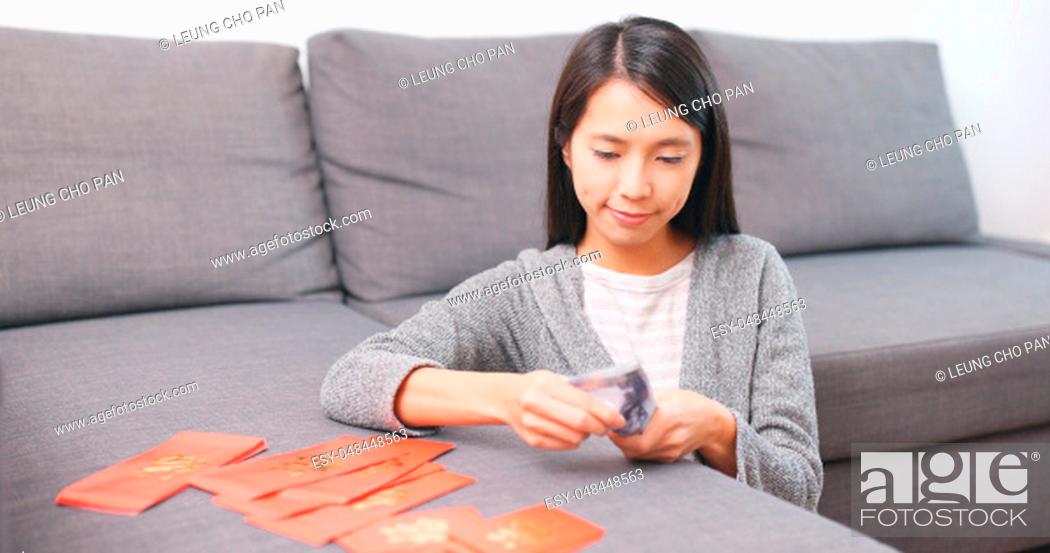 Stock Photo: Woman putting money banknote into red packet at home.