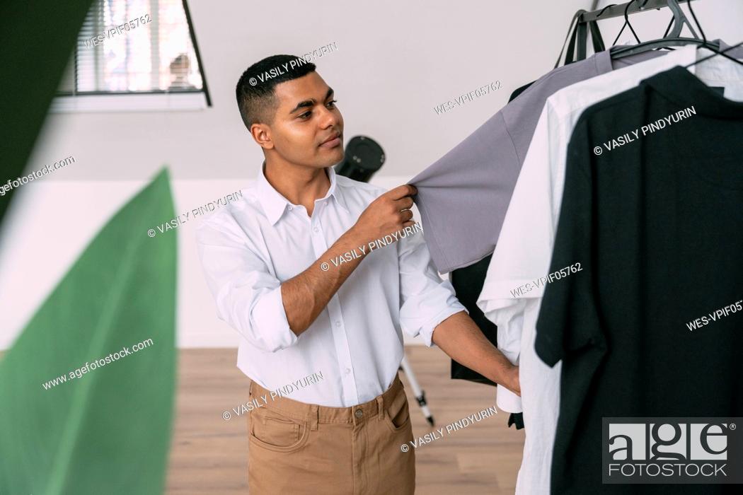Stock Photo: Young man choosing t-shirt from clothing rack at home.