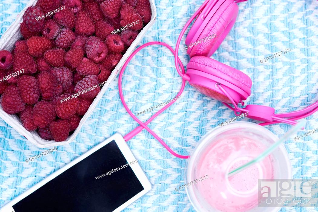 Stock Photo: Box of raspberries, smoothie, smartphone and pink headphones on blanket.