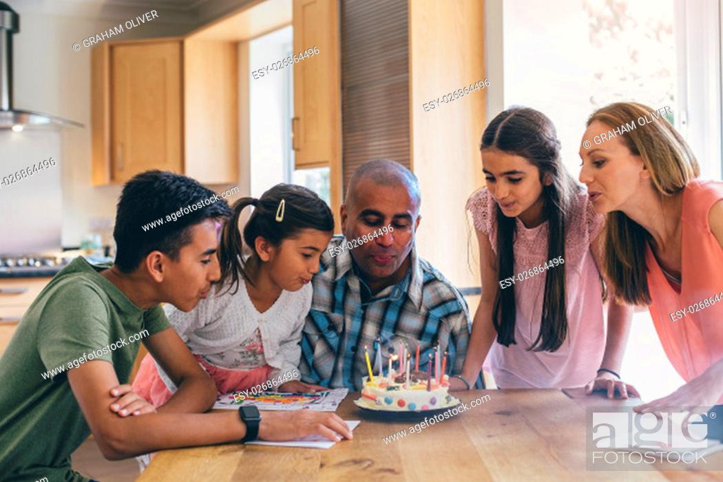 Stock Photo: Happy family celebrating the fathers birthday. They are all helping him blow out the candles on his cake.