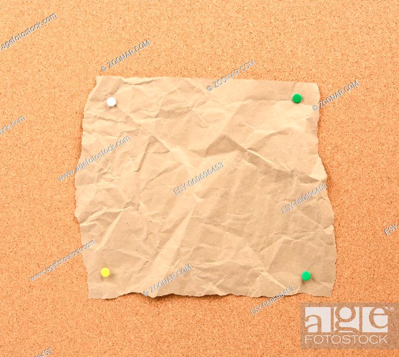 Stock Photo: brown piece of torn paper pinned with iron buttons on a brown cork board, copy space.