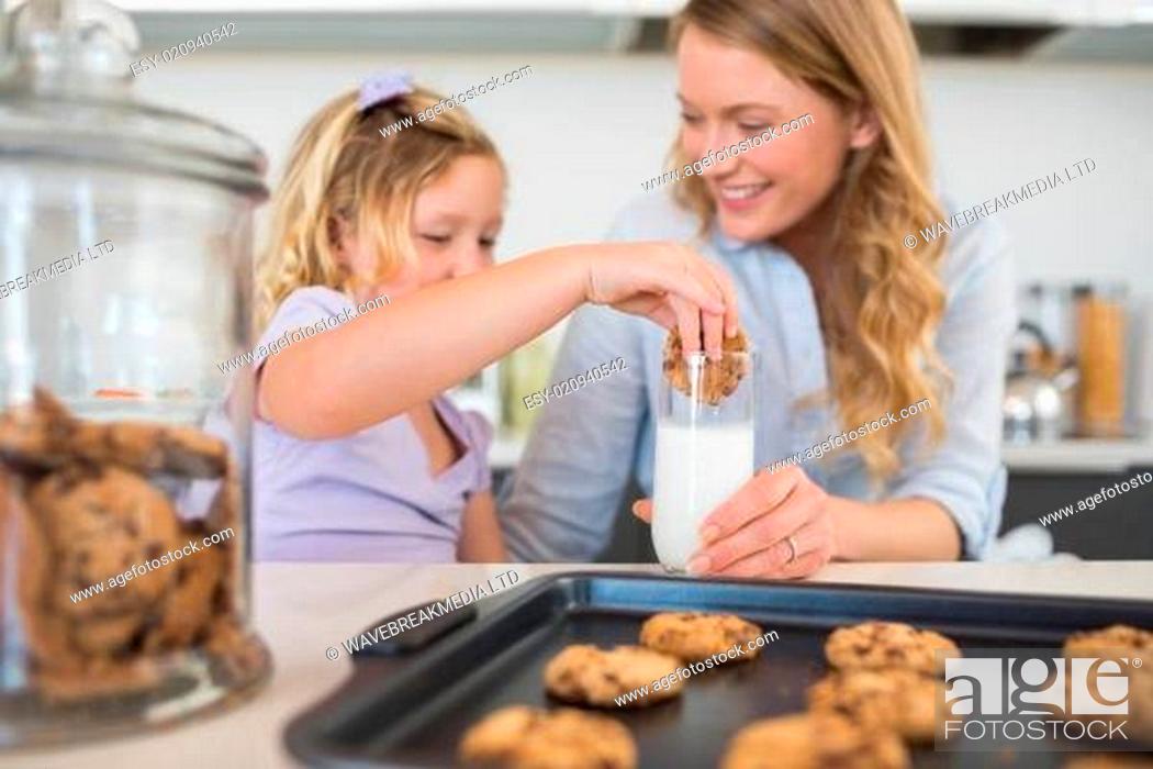 Stock Photo: Woman with daughter dipping cookie in milk.