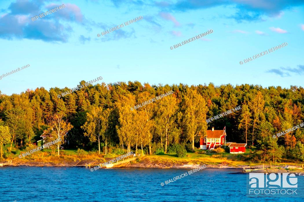 Stock Photo: Oslo, Ostlandet / Norway - 2019/09/02: Panoramic sunset view of Lindoya island on Oslofjord harbor with summer cabin houses at wooded shoreline in early autumn.
