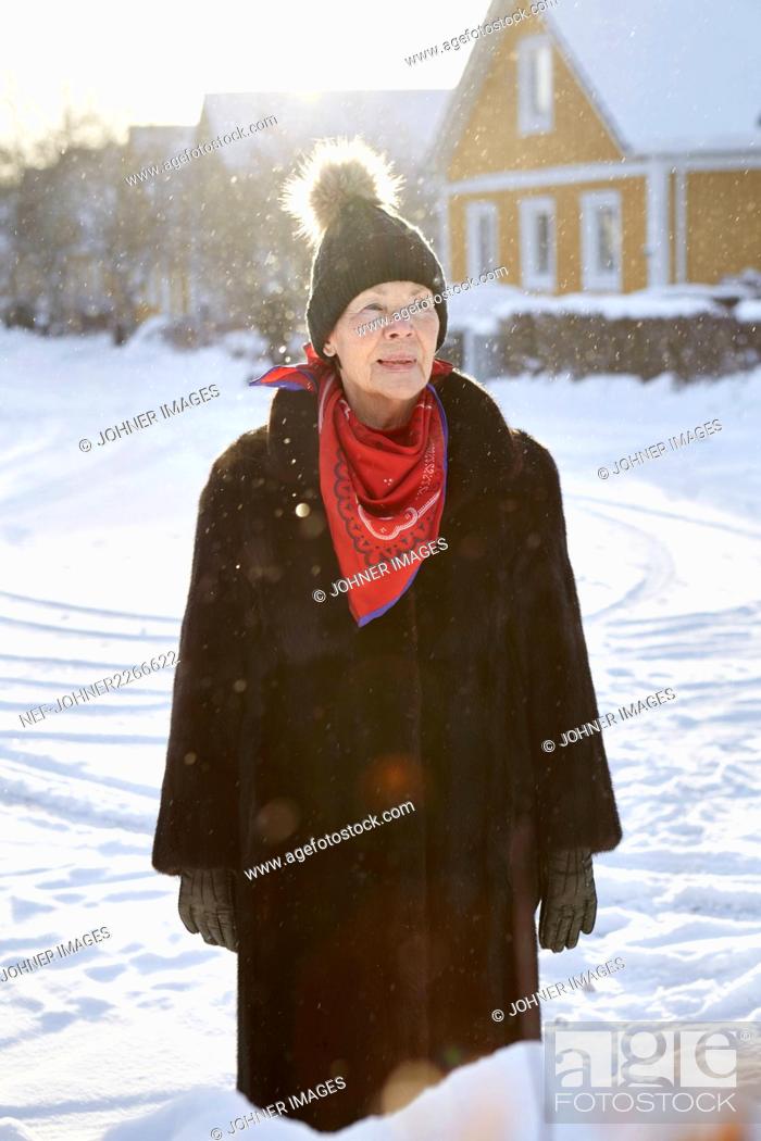Stock Photo: Senior woman standing in front of house in winter.