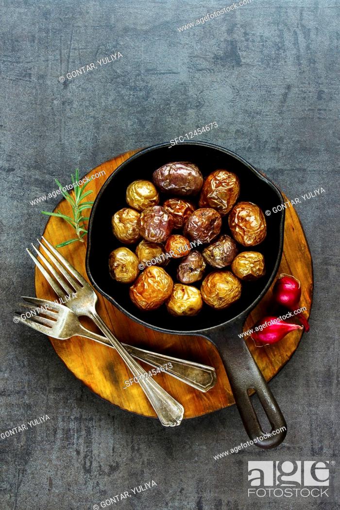 Photo de stock: Tasty fried baby potatoes in vintage cast iron pan on wooden board over black concrete background.
