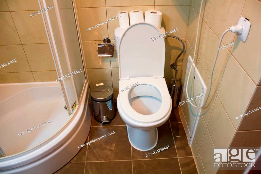 Stock Photo: White toilet in it are three rolls of toilet paper near a shower is situated.