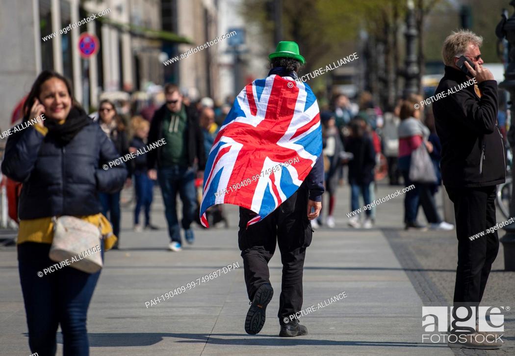 Stock Photo: 09 April 2019, Berlin: A man with a national flag of the United Kingdom on his back crosses a street in the city centre. Chancellor Merkel today received.