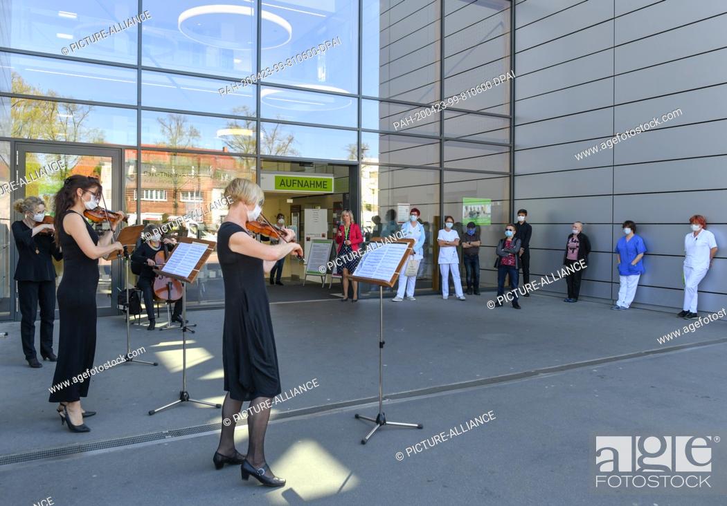 Stock Photo: 23 April 2020, Brandenburg, Cottbus: Musicians from the Cottbus State Theatre play for patients in front of the main entrance to the Carl-Thiem-Klinikum (CTK).