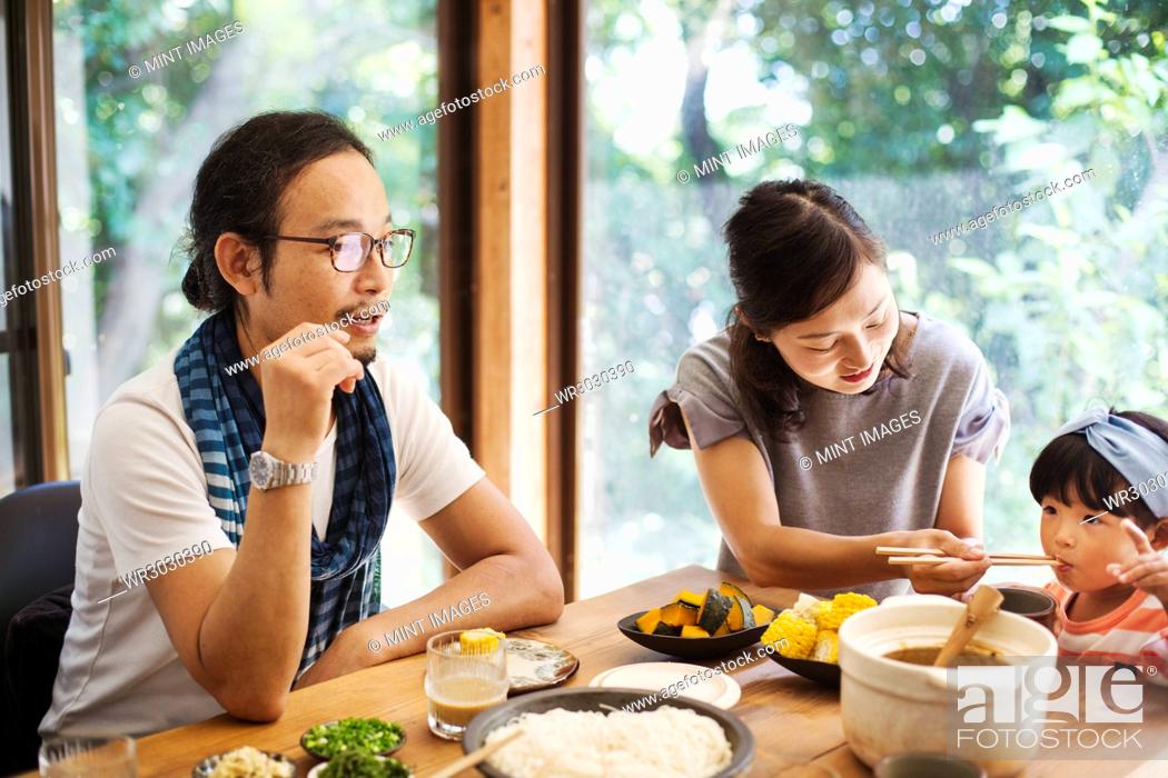 Stock Photo: Man, woman and young girl sitting round a table with bowls of food, eating together.