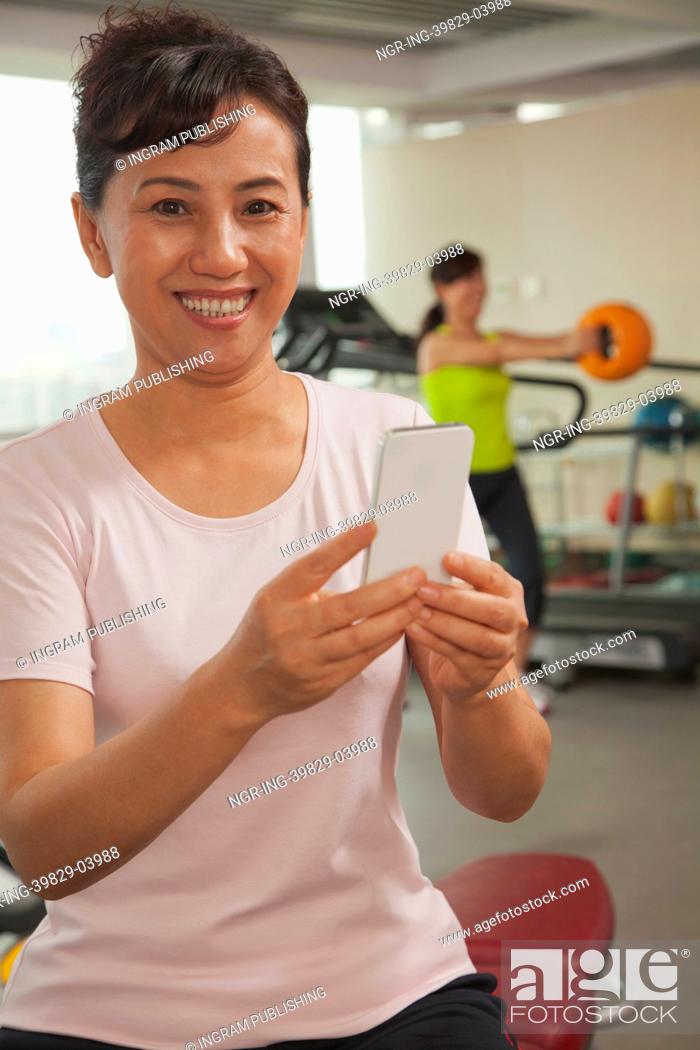 Stock Photo: Mature woman using her cell phone in the gym, looking at the camera.