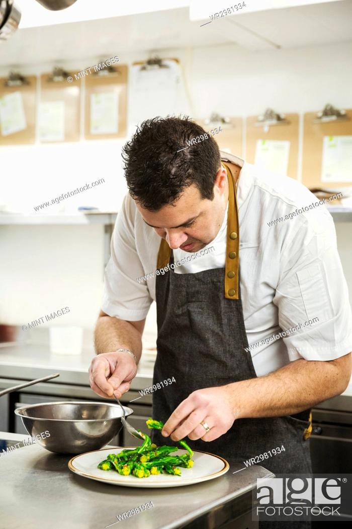 Imagen: Chef standing in the kitchen in a small hotel, plating up a dish of vegetables.