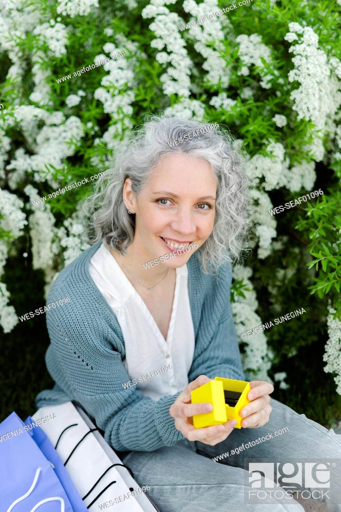 Imagen: Happy woman holding yellow gift box in front of plant.