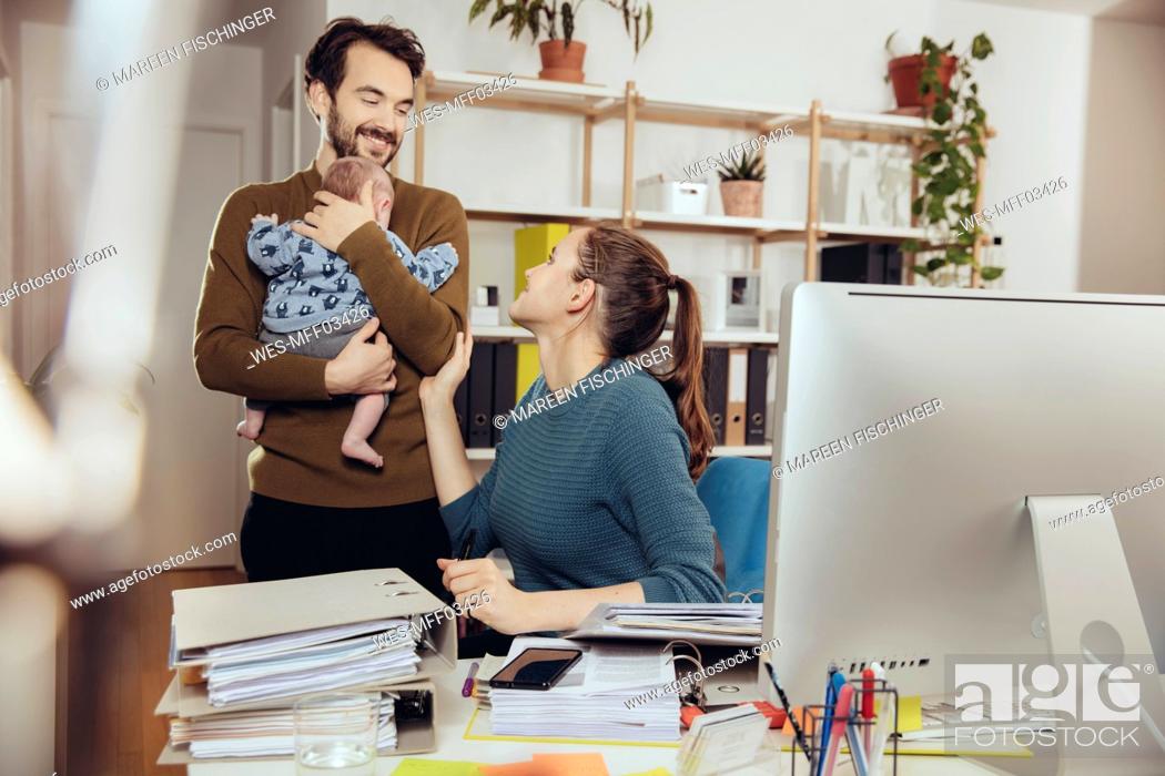 Stock Photo: Smiling mother at desk looking at father holding baby in home office.