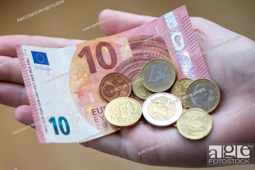 Stock Photo: ILLUSTRATION - 09 April 2021, Bavaria, Nuremberg: A woman holds notes and coins in her hand. The savings rate in Germany was at a record high of 16.