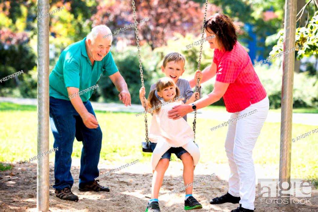 Stock Photo: Family Having Fun With Kids Having Ride On Swing In The Park.