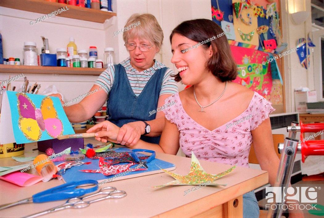 Stock Photo: Carer assisting teenage girl to use paintbrush during art lesson in residential respite care home,.