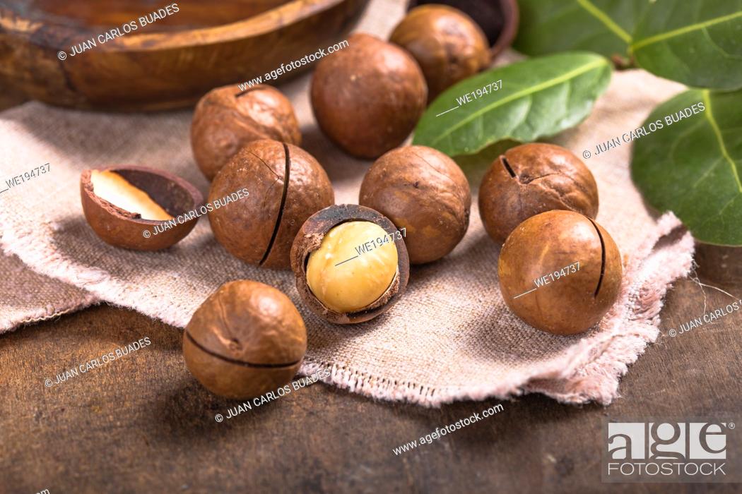 Stock Photo: Pile macadamia nuts open kernels and shells in burlap bag on wooden background.