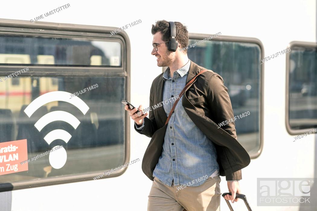Stock Photo: Smiling young man with headphones and cell walking along train with wifi symbol.