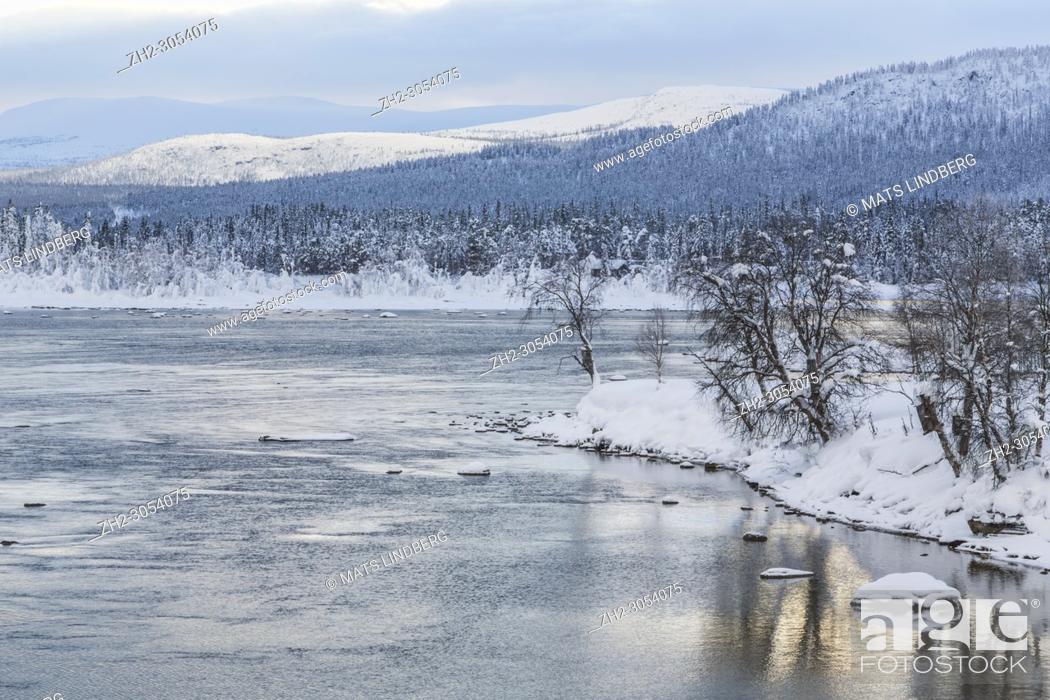 Stock Photo: Winter landscape in Tjåmotis with mountains in background, sun shining over the mountains, creek with open water, sky with nice colors reflecting in the water.
