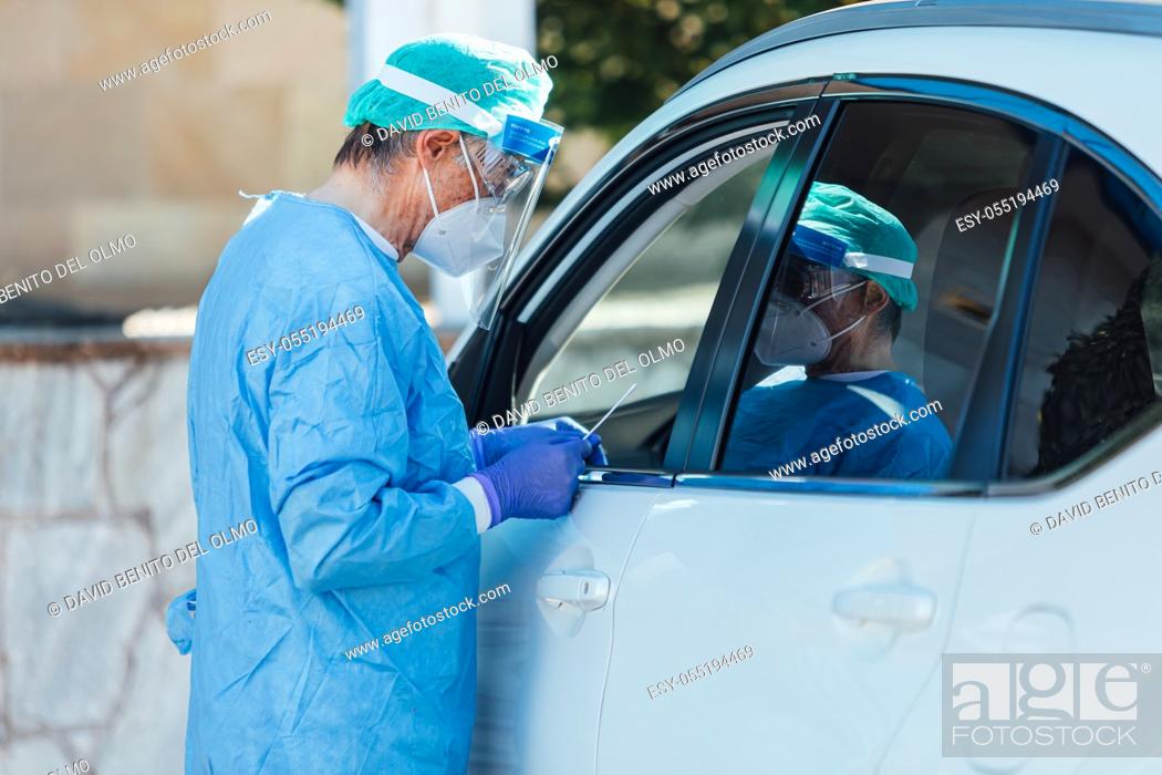 Stock Photo: Medical personnel wearing a PPE, performing PCR with a swab in their hand, on a patient inside his car to detect if he is infected with COVID-19.