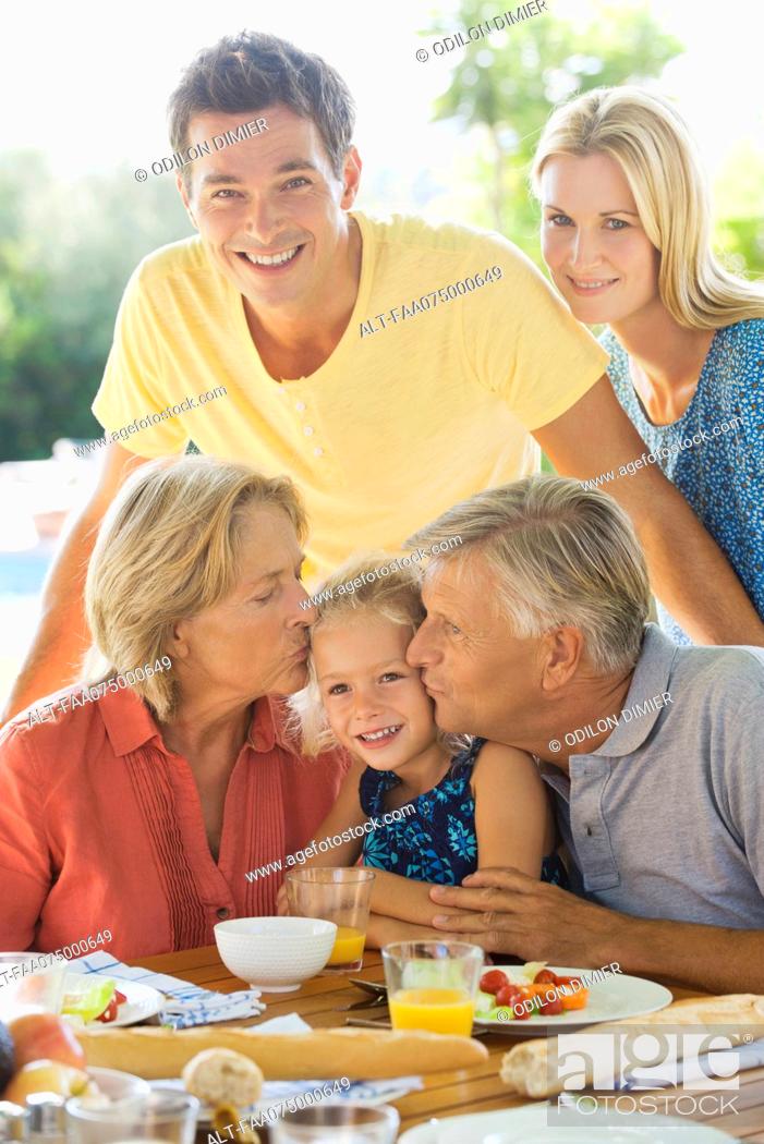 Stock Photo: Family having breakfast outdoors, grandparents kissing granddaughter's cheeks, portrait.