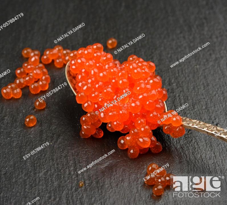 Stock Photo: red caviar of chum salmon in a metal spoon on a black background, close up.