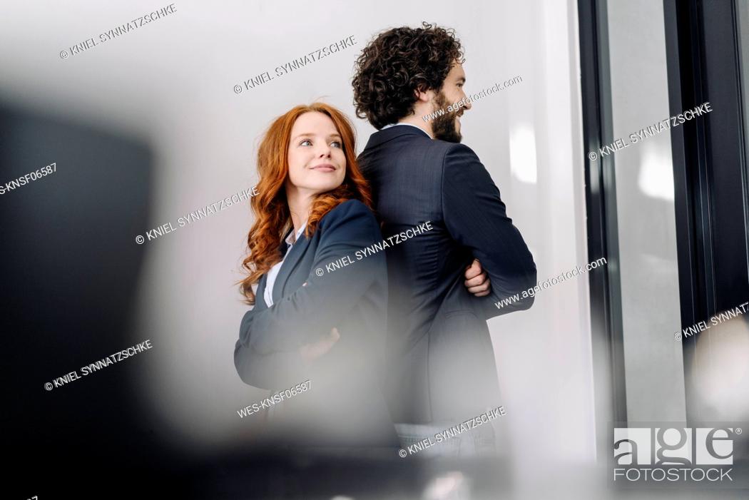 Stock Photo: Confident businessman and businesswoman standing back to back in office.