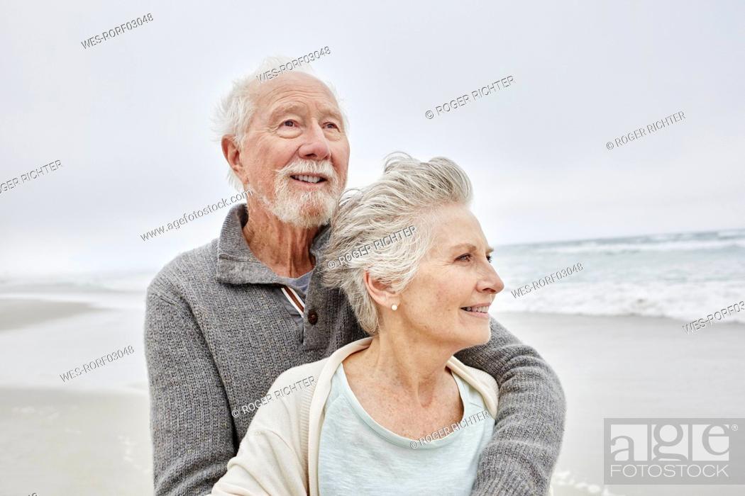 Photo de stock: Happy senior couple standing smiling on windy beach.