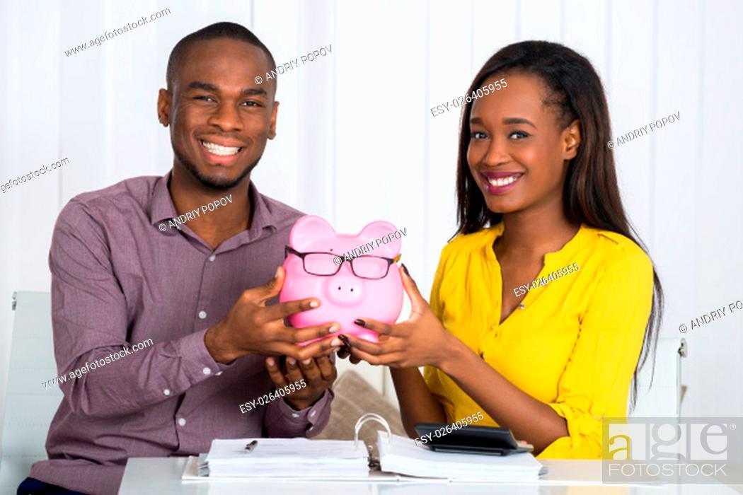 Stock Photo: Happy Couple Holding Piggybank With Invoice And Calculator On Desk.