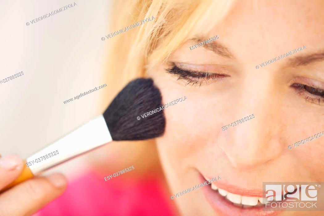 Stock Photo: Beautiful young woman applying foundation powder or blush with makeup brush.