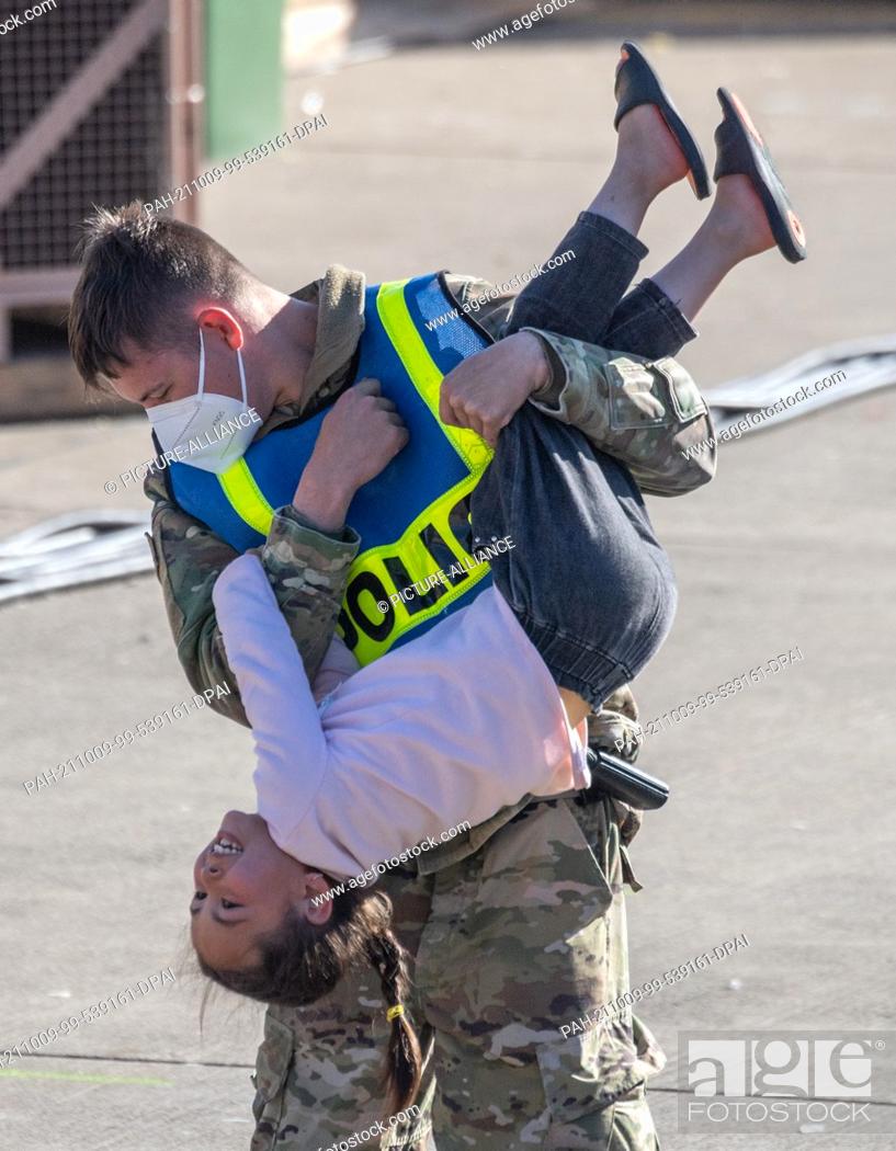 Stock Photo: 09 October 2021, Rhineland-Palatinate, Ramstein: A US military policeman twirls a little girl from Afghanistan through the air at the US airbase in Ramstein for.