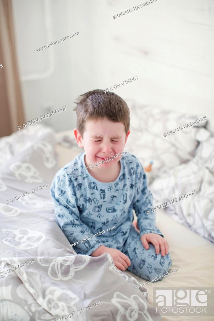 Imagen: Crying boy sitting on bed at home.