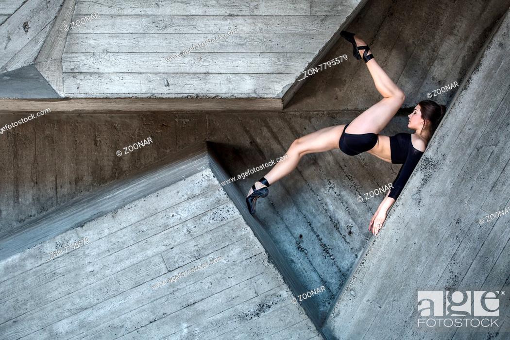 Stock Photo: Flexible dancer posing lies between the complex geometry of concrete walls. Dancer lying on his back resting his toes in the opposite wall.