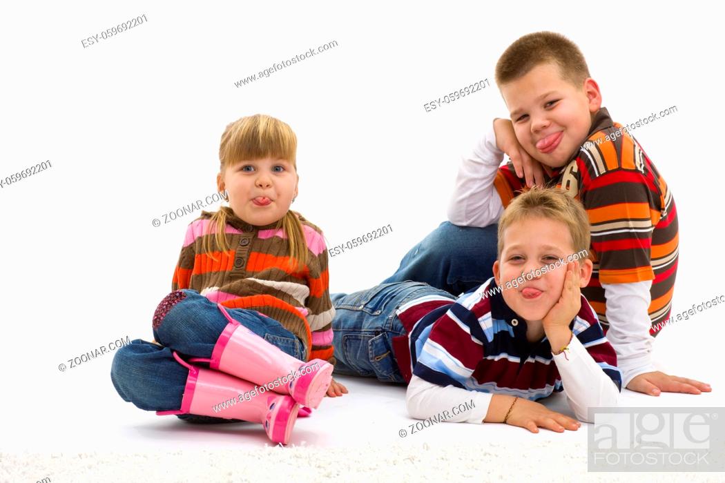 Stock Photo: Group of 3 happy children lying on floor wearing colorful, trendy clothes, sticking their toungues out. Isolated on white background.