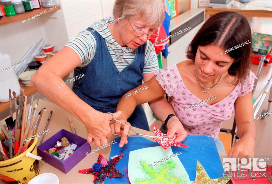 Stock Photo: Carer assisting teenage girl to use dual control training scissors in residential respite care home,.
