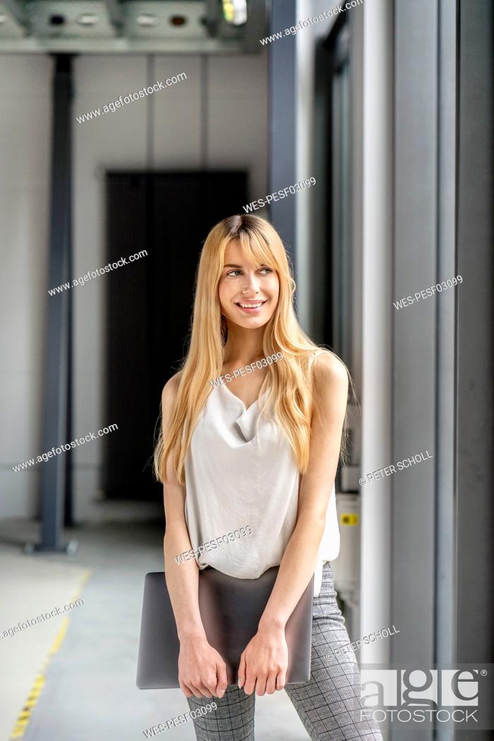 Stock Photo: Young blond businesswoman holding laptop at workplace.