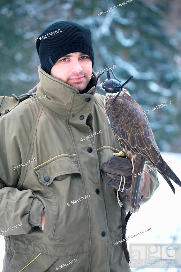 Stock Photo: Young handsome man holding a falcon on his arm.