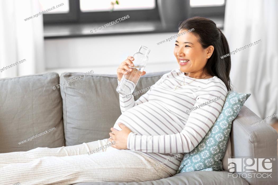Stock Photo: pregnant woman with water in glass bottle at home.