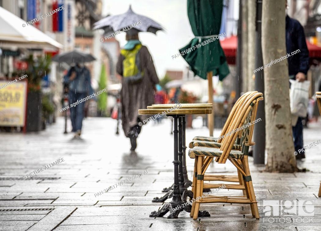 Stock Photo: 17 May 2021, Hessen, Bad Homburg: Tables and chairs remain empty in a rain shower in downtown Bad Homburg. In five Hessian counties as well as the city of.