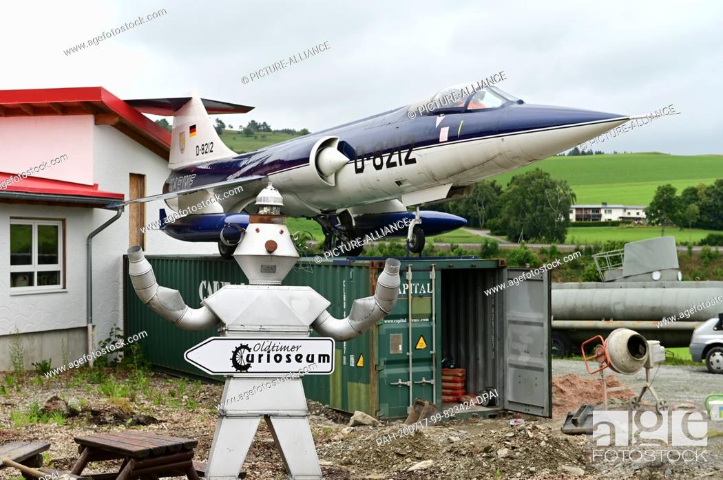 Stock Photo: 10 July 2020, Hessen, Willingen: A scrap robot and a Lockheed F-104 Starfighter are parked in front of the Curioseum. The Curioseum in Willingen is one of.