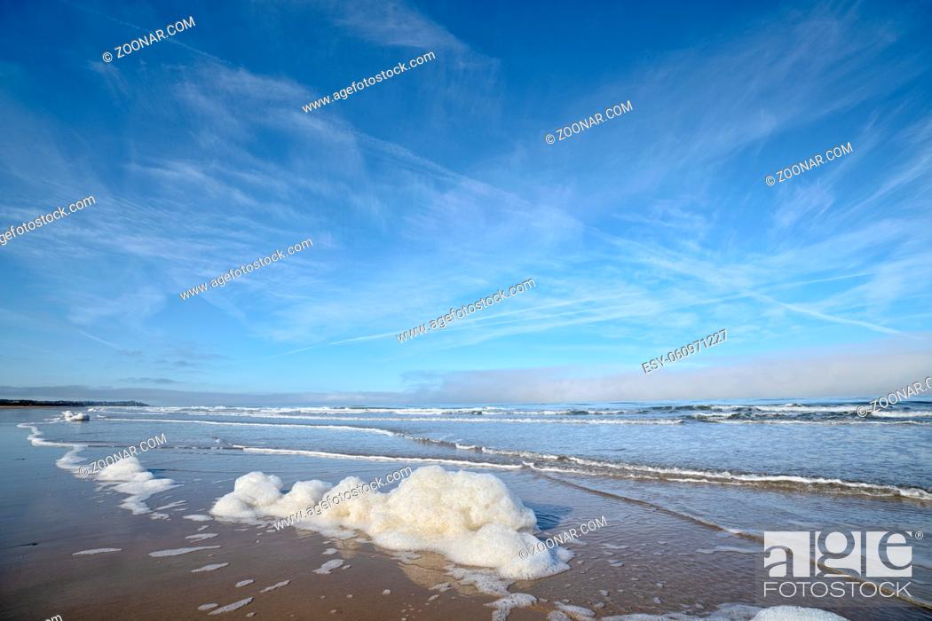 Stock Photo: Foam on the beach by the ocean under a blue sky with waves coming in.