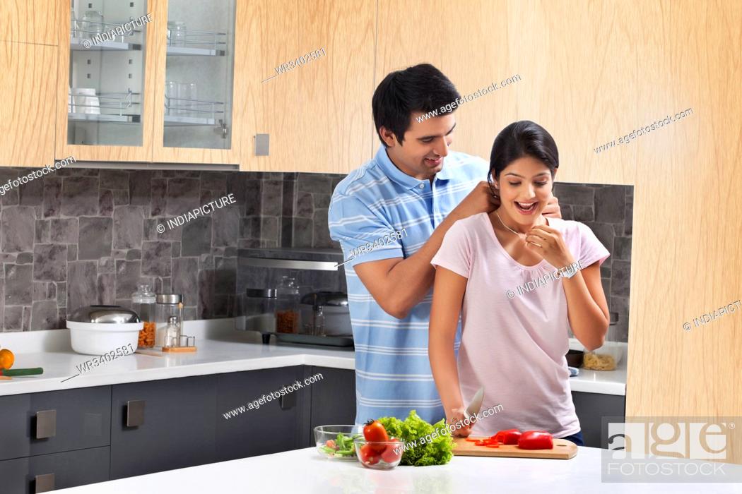 Stock Photo: Loving man putting necklace on surprised woman in kitchen.
